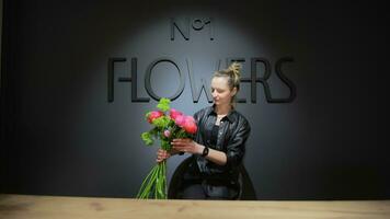 The florist examines the bouquet, then looks at the camera. A florist girl in a flower shop looks at a freshly made bouquet at the counter. The concept of floristry video