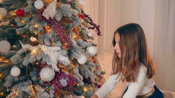 un pequeño niña decora un Navidad árbol. de cerca de para niños manos pegajoso a un plata pelota en un Navidad árbol. nuevo año decoraciones video