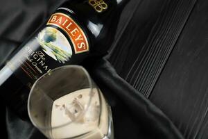 KYIV, UKRAINE - MAY 4, 2022 Baileys original alcohol bottle on wooden table with black fabric photo