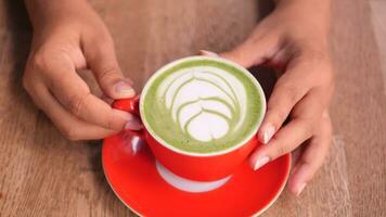 women holding a matcha latte in a red color cup on table video