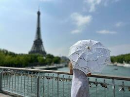 the perfect backdrop for any story about Paris a slender girl looks up at the Eiffel Tower but all we see is a parasol and a blue sky the photo is calm and interesting like a picture