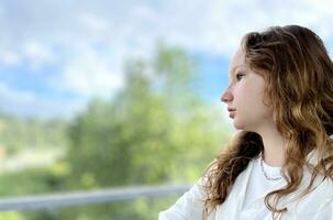 European girl with blond long hair in a white shirt rides in a skytrain she sadly looks out the window she is sad waiting for her A long road outside the window flashes nature houses Vancouver Surrey photo