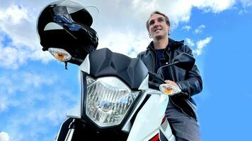 masculino motorista se sienta en un motocicleta en contra el antecedentes de naturaleza y montaña él en un cuero chaqueta en el bigote daliniano de un motocicleta es vistiendo un casco foto