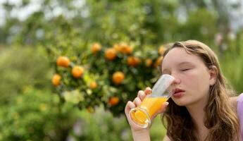 the girl drinks orange juice against the background of a tangerine tree, it can be orange juice tangerine mango she drinks greedily and really likes the juice delicious everywhere greens and summer photo