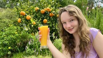 the girl drinks orange juice against the background of a tangerine tree, it can be orange juice tangerine mango she drinks greedily and really likes the juice delicious everywhere greens and summer photo