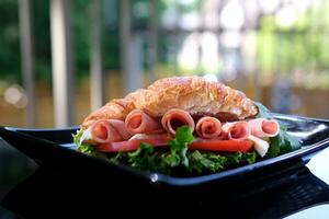 seis piezas de tocino arrollado dentro un emparedado cuerno lechuga hojas queso Brie queso desayuno elegante comida en un negro plato restaurante servicio servicio tomate al aire libre verano foto