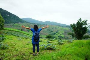 Asian woman with backpack is spread arms on terrace paddy rice fields on mountain for freedom life, Chiangmai Province of Thailand. People for travel in greenery tropical rainy season concept photo