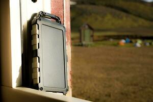 Rugged power bank battery with solar cell charging in the sun, nature and tents of campsite in the background photo