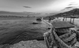 Black and white landscape with selective focus on rope anchoring fishing boat at the pier. photo