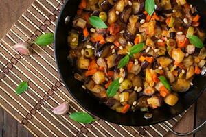 caponata italiana con sartén sobre un fondo de madera foto