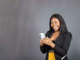 smiling young Black woman wear black suit using smartphone app isolated on grey studio background copy space photo