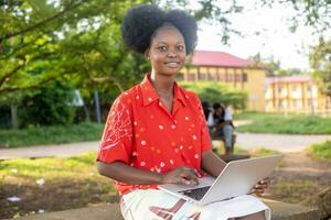 pretty young black lady sitting alone with her laptop computer outdoor in a park smiling photo