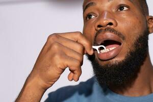 negro hombre utilizando un seda floja a limpiar su dientes foto