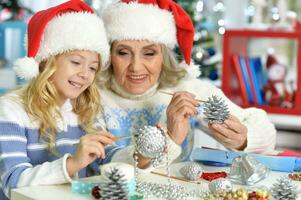 Grandmother and granddaughter in Santa hats making New Year's decorations photo