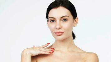 Close-up beauty portrait of young woman with smooth healthy skin, she gently touches her face with her fingers on light grey background and smiles. Skincare concept photo