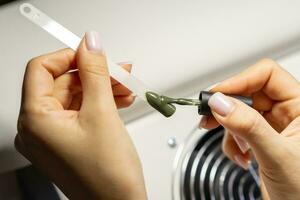 A manicurist applies gel nail polish to empty tips as a sample photo