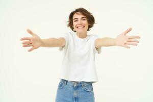 Portrait of beautiful, friendly woman stretching hands, hugging, extending arms for cuddle, embracing someone, standing against white background photo