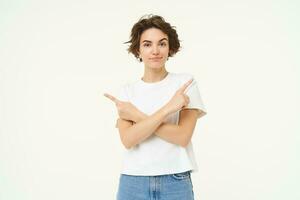 Puzzled woman makes choice, points fingers left and right, deciding, confused what to pick, stands over white studio background photo