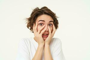 Image of girl screams and looks scared, hides face with hands, stands over white background photo