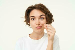 Close up portrait of brunette woman zip her lips, shows gesture to keep mouth shut, makes promise to safe someones secret, stands over white background photo