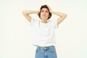 Portrait of woman in panic, grabs her head, feeling troubled, has big problem, stands anxious against white backgrond photo