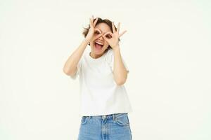 Portrait of carefree european woman, showing glasses with hands over eyes and smiling, posing over white background photo