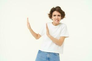 Portrait of woman avoiding someone, shows block hands gesture and refusing from something bad, standing over white background photo