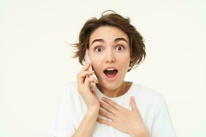 Portrait of woman with surprised face, answers phone call and looks excited, amazed by big news, stands over white background photo