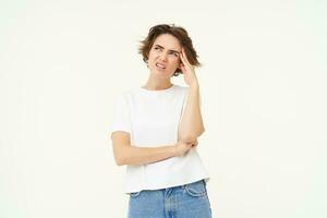 Portrait of woman looking troubled, thinking and frowning, having complicated situation, standing over white studio background photo
