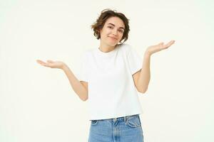 Woman shrugs her shoulders, looks clueless, doesnt know anything, stands confused against white background photo