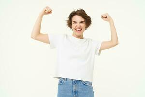 Portrait of happy and confident girl shows muscles, flexing biceps and smiling, posing over white background photo