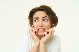 Close up of scared brunette woman, shaking from fear, looking concerned and frightened, standing over white studio background photo