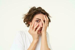 Close up of brunette woman hiding her face, screams and looks frightened, horrified by something, standing scared against white background photo