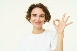 Close up of smiling, happy young woman shows zero, okay ok gesture, approve something good, standing over white background photo