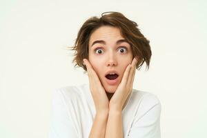 Portrait of girl with surprised face, makes shocked expression, stands over white background photo