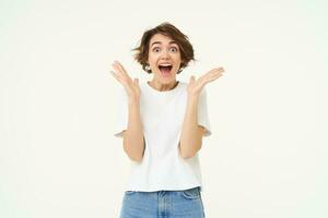 Image of woman with surprised face, amazed, says wow, claps hands and looks excited, stands over white background photo