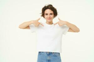 Image of confident, happy young woman, pointing at herself with smiling face, self-assured, standing over white background photo