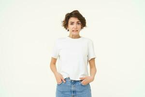 Portrait of girl with concerned face, looks unsure, grimacing, looking confused, standing over white background photo