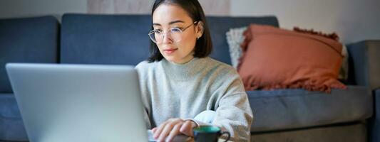 Self employed young korean woman working on remote, typing on laptop, studying at home in living room photo