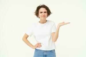 So what. Frustrated, upset young woman, raises one hand and shrugs, looking confused, cant understand something, standing over white background photo