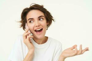 Portrait of happy, chatty young woman talking on mobile phone, using smartphone, calling someone, standing over white studio background photo