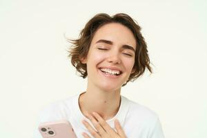 Portrait of young woman standing with pink mobile phone, using smartphone app, doing online shopping, paying for something using application, standing over white background photo