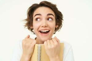 Portrait of happy woman with planner, holding notebook, reading notes and smiling, standing over white background photo