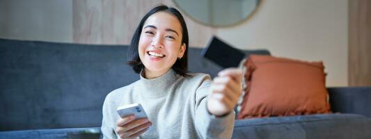 Smiling asian girl with smartphone and credit card, does her shopping online, uses mobile phone to order home delivery photo