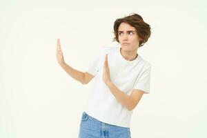 Portrait of woman avoiding someone, shows block hands gesture and refusing from something bad, standing over white background photo