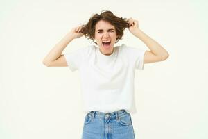 Woman screams, pulls out her hair and shouts, stands frustrated, angry and pissed-off, stands over white studio background photo