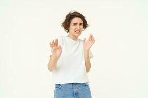 Young reluctant woman steps back, raises hands to refuse, rejects something disgusting, reaction of aversion and dislike, isolated over white background photo