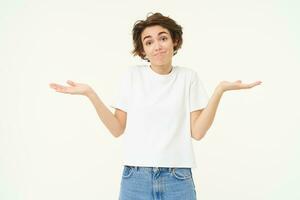 Woman shrugs her shoulders, looks clueless, doesnt know anything, stands confused against white background photo