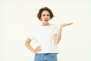 Portrait of woman complaining, raising hand up with frustration, looking angry, standing over white background photo