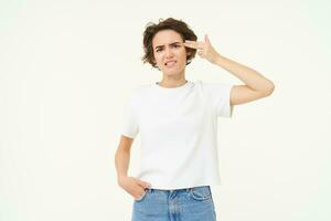 Portrait of woman holding fingers near temple, beeing fed up, annoyed by something, standing tired against white background photo